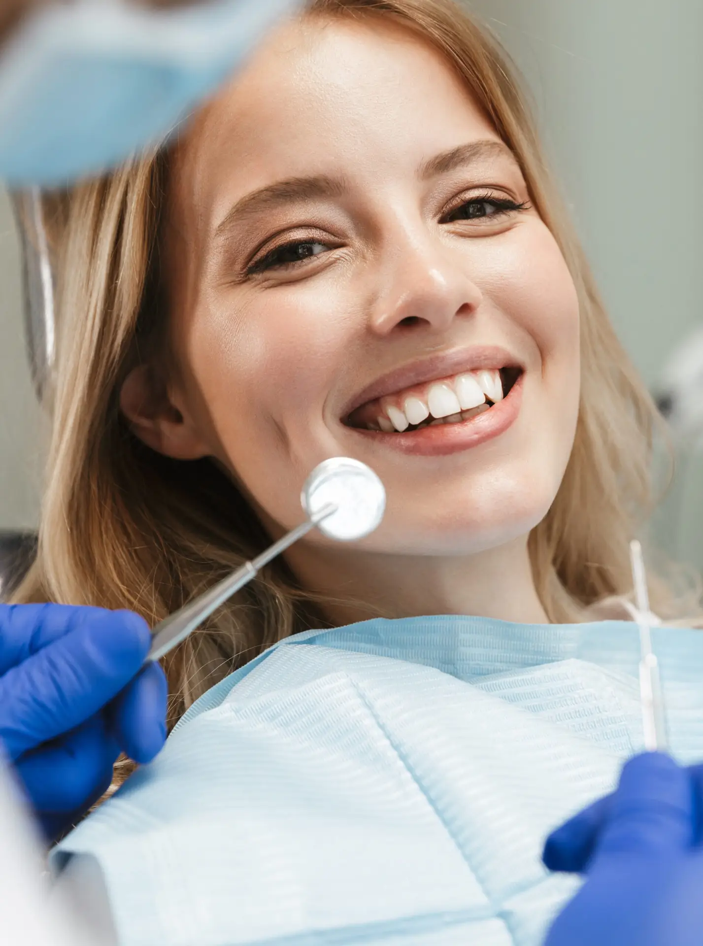 Stock image of a satisfied young woman sitting in the dental chair during a cleaning by the dentist.